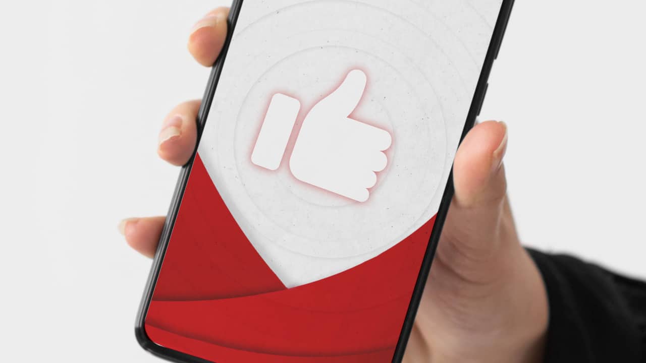 Image of a hand holding a smart phone with an image of a large Thumbs Up emoji on the screen.